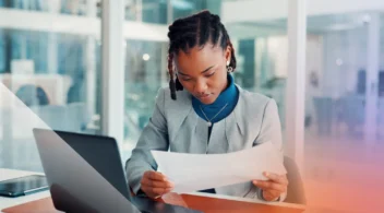 Professional female salesperson reviewing documents at a desk with a laptop.